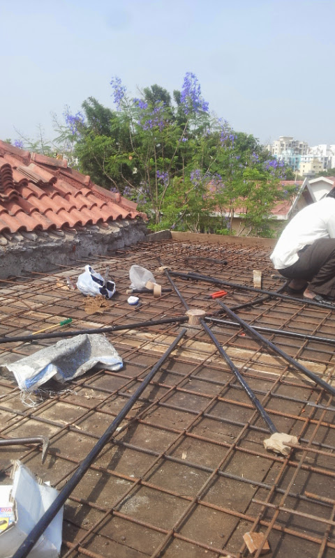 Rooftop rebar construction with workers and a jacaranda tree in the background