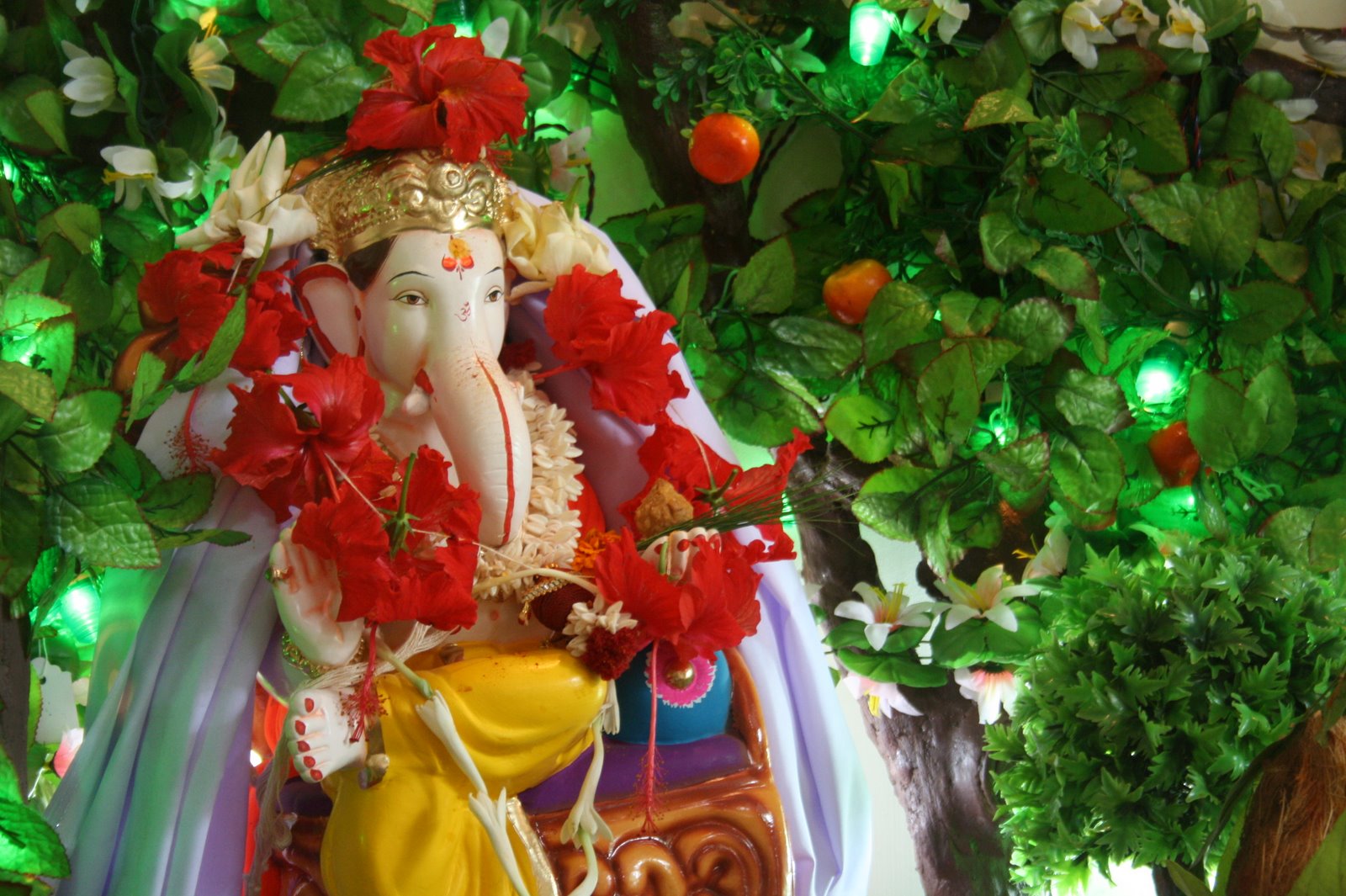Refined Ganpati installation with a Ganesh idol dressed in a red hibiscus garland against a canopy of green leaves and flowers