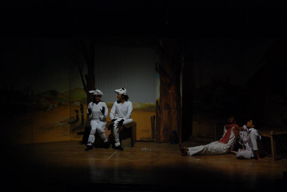 Wide stage shot: farmer and wife seated in darkness with a single red light